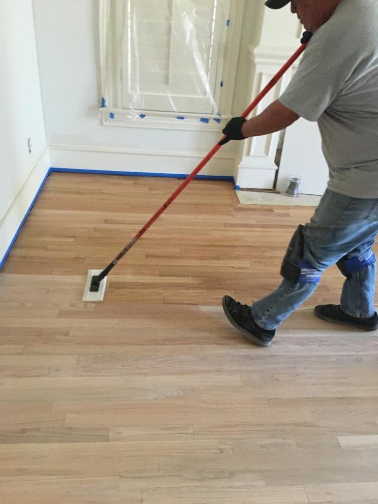Applying a finish coat to a refinished hardwood floor in a DFW home (worker actively applying finish to hardwood floor)