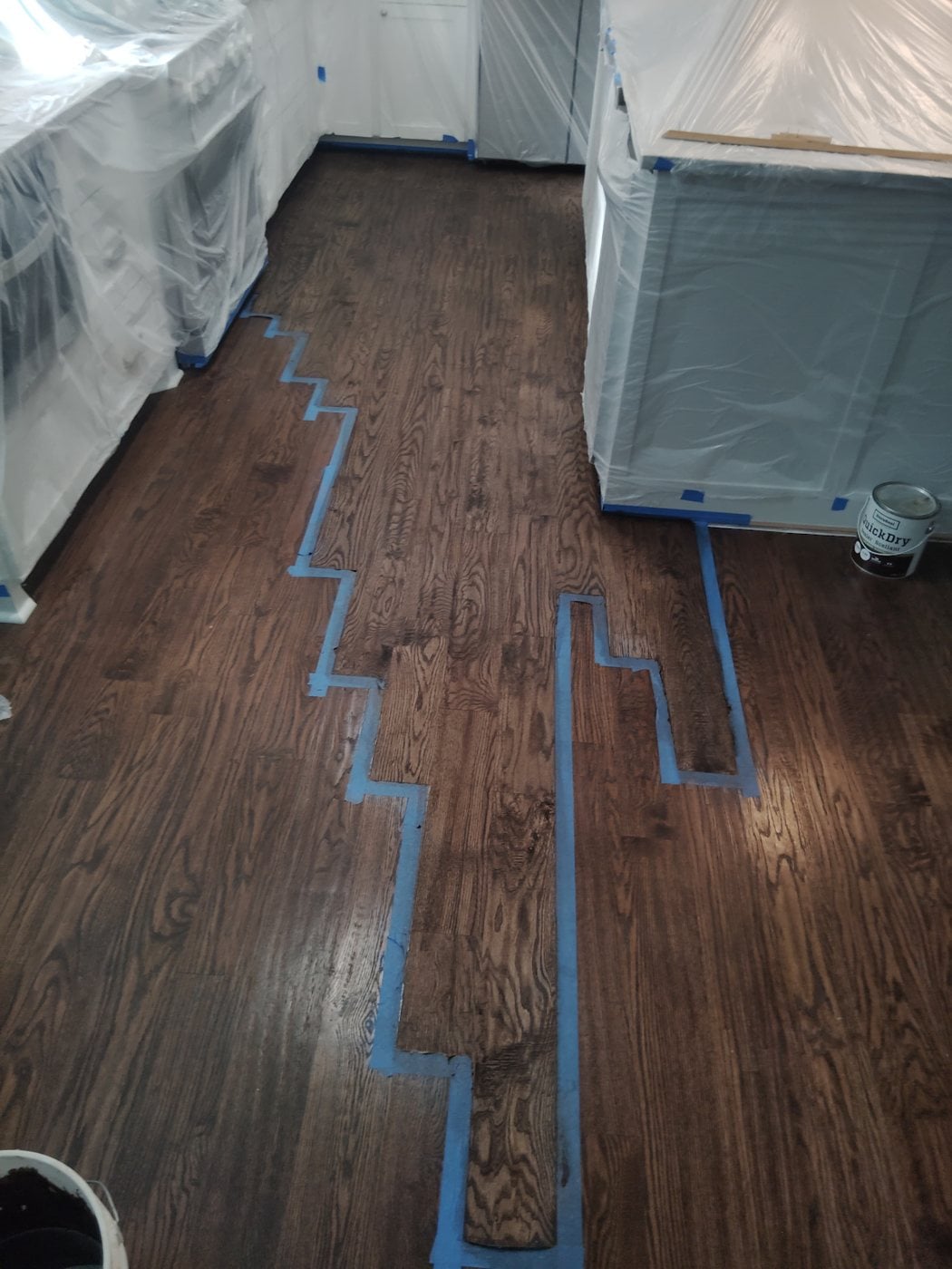 Hardwood floor repair in progress with damaged boards removed (floor repair in progress with tape and plastic)